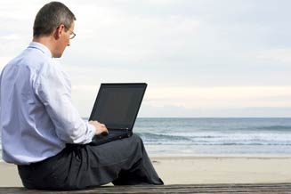 Man using laptop to access digital files on beach.